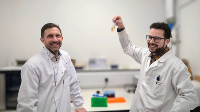 Dos hombres con batas de laboratorio, uno sosteniendo un tubo de ensayo.