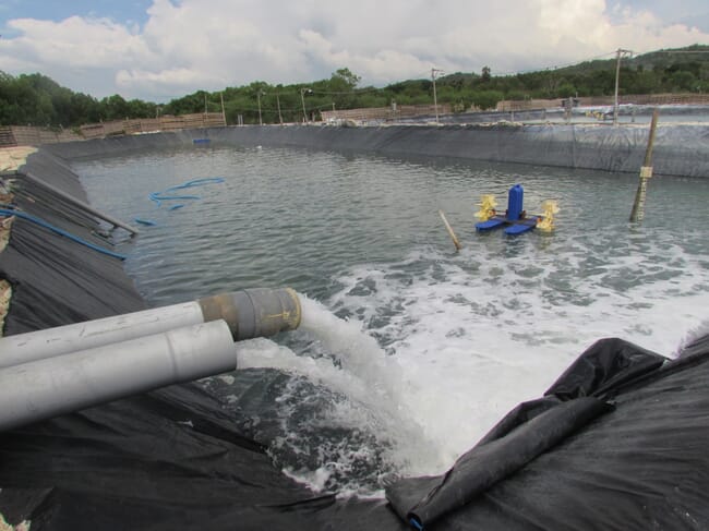Two pipes pumping water into a shrimp pond with a plastic lining